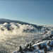 Photo of a view of a mountain summit: fog, evergreen trees, and snow.